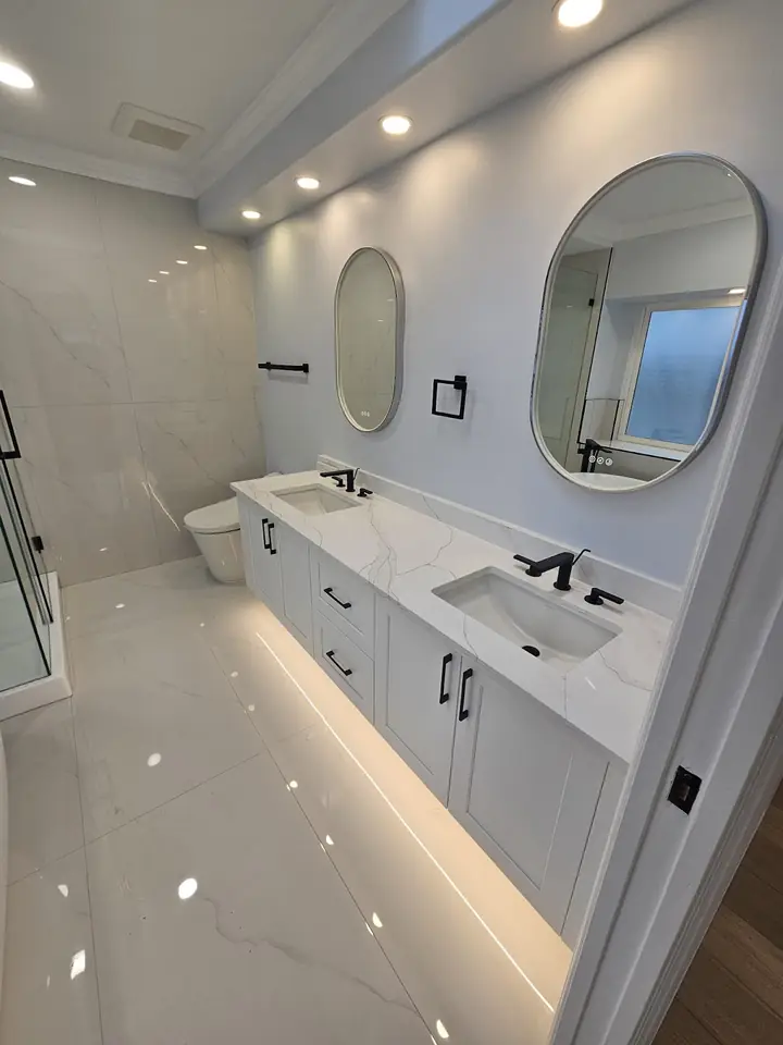 Capilano bathroom renovation: white double vanity, oval mirrors and lighting along the toe kick