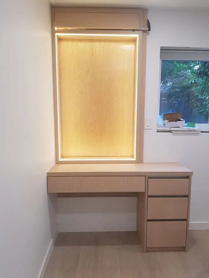 Built-in desk with drawers below a lit mirror niche in a Delbrook home